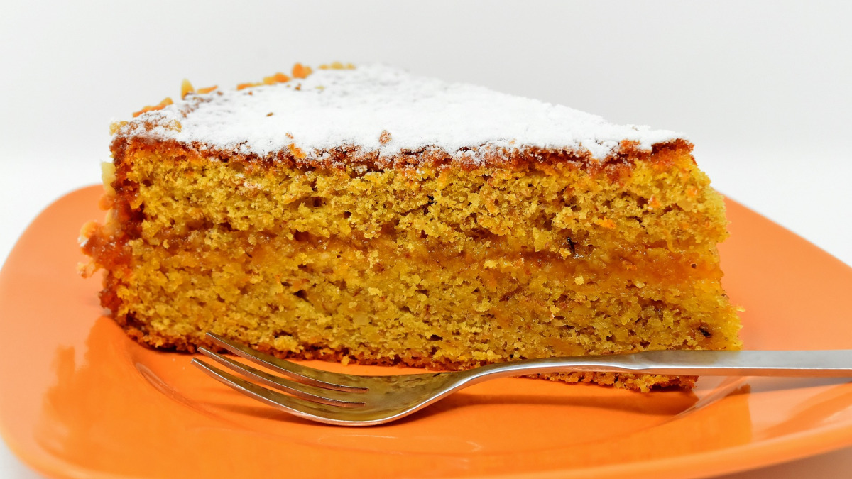 Fatia de bolo de cenoura com cobertura de açúcar de confeiteiro em prato laranja