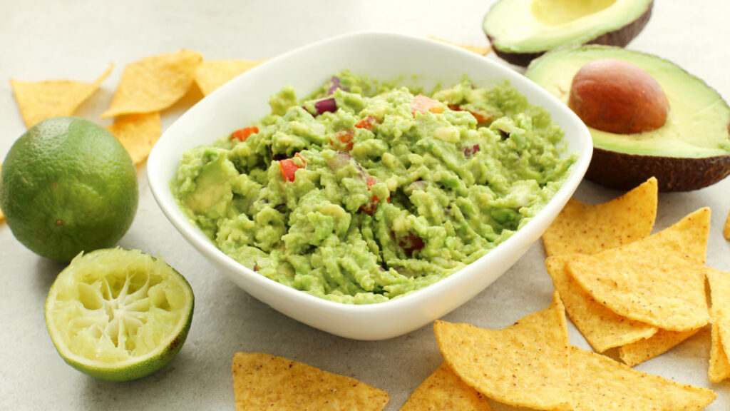 Guacamole servida em travessa branca com nachos ao lado