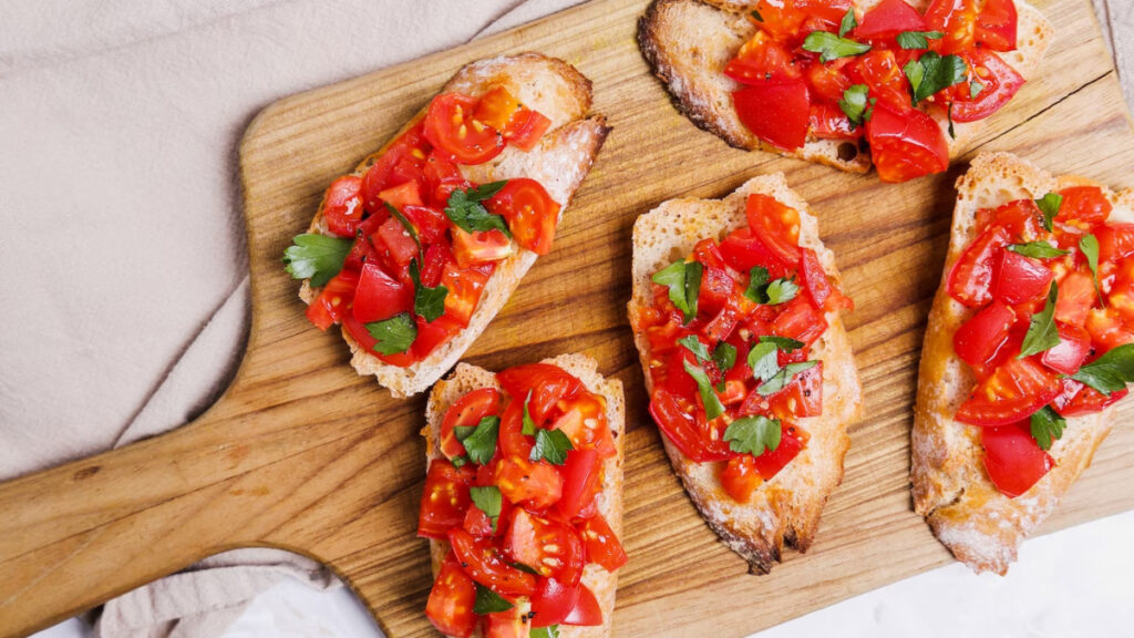 5 bruschettas de tomate e manjericão em cima de tábua de madeira de cozinha