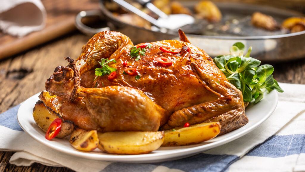 Frango assado com batatas em um prato branco em cima da mesa