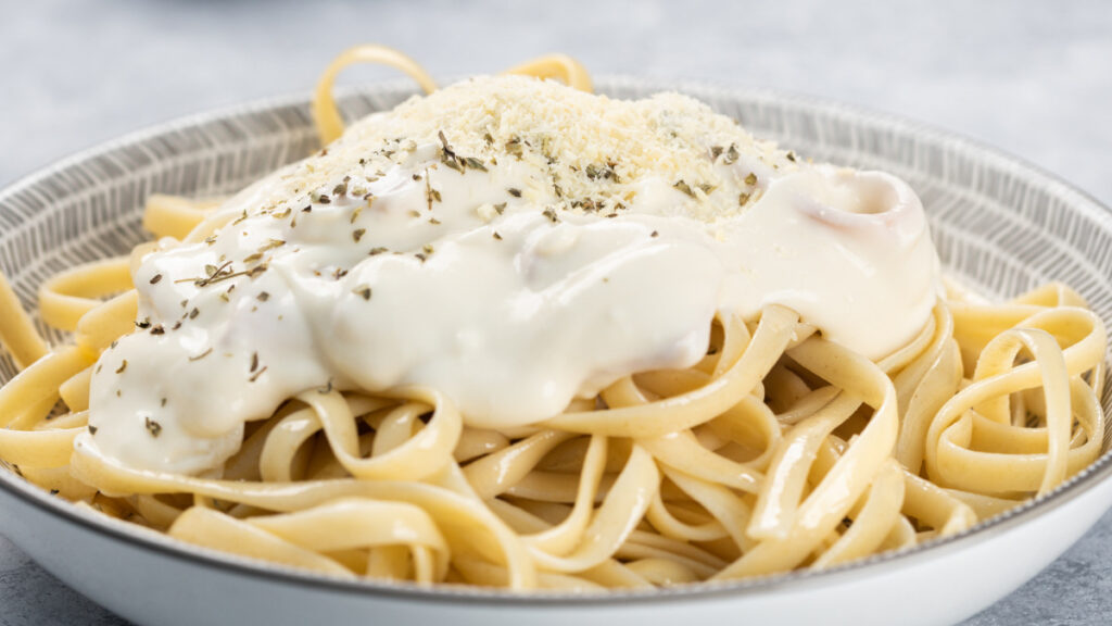 Macarrão ao molho branco dentro de prato redondo em cima da mesa de mármore