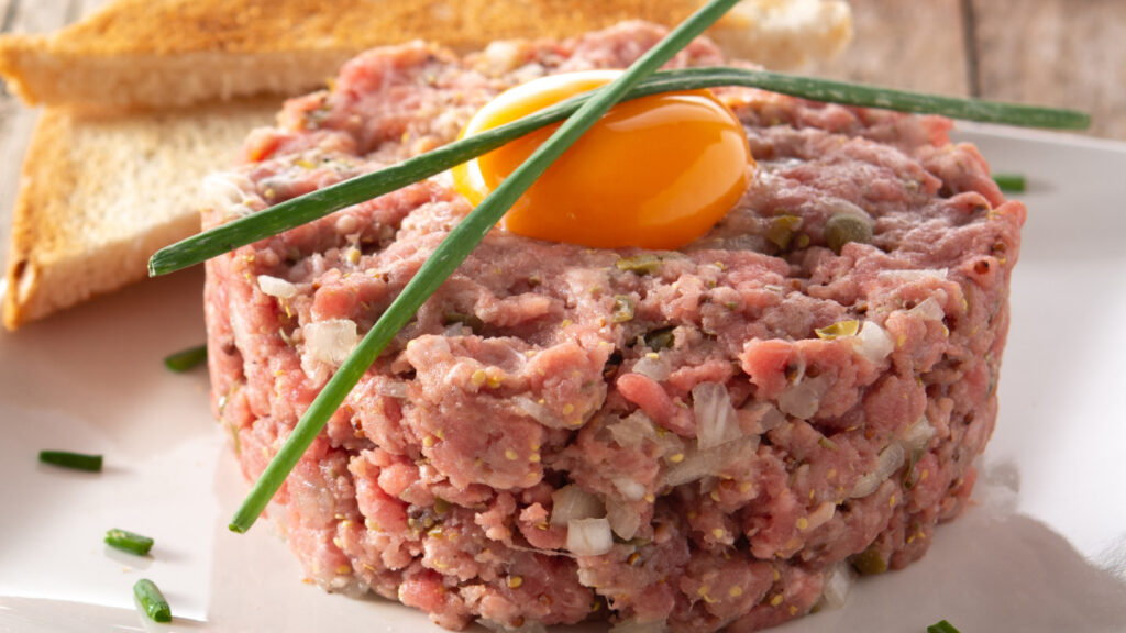 Steak tartare com uma gema de ovo por cima, ambos dentro de um prato branco