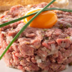 Steak tartare com uma gema de ovo por cima, ambos dentro de um prato branco