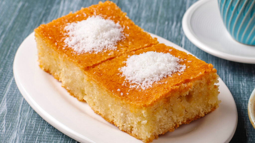 Dois pedaços de bolo de arroz com coco ralado em cima de prato branco