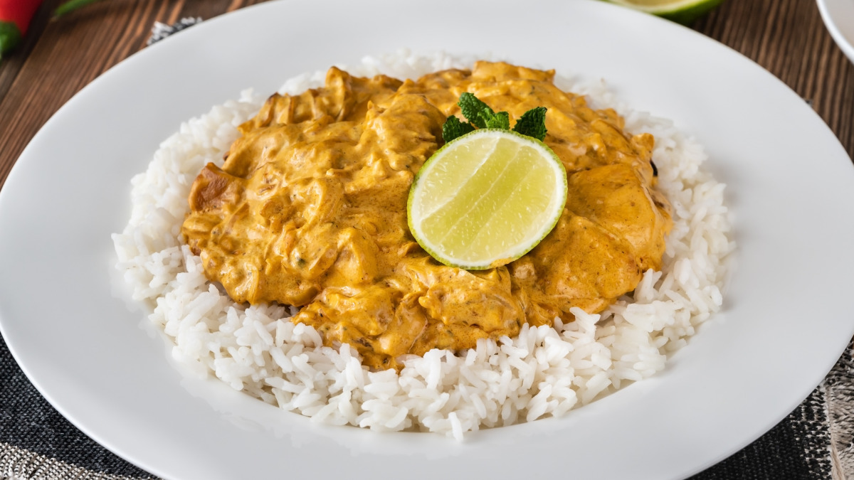Frango ao curry com creme de ricota sobre um arroz branco em um prato redondo branco