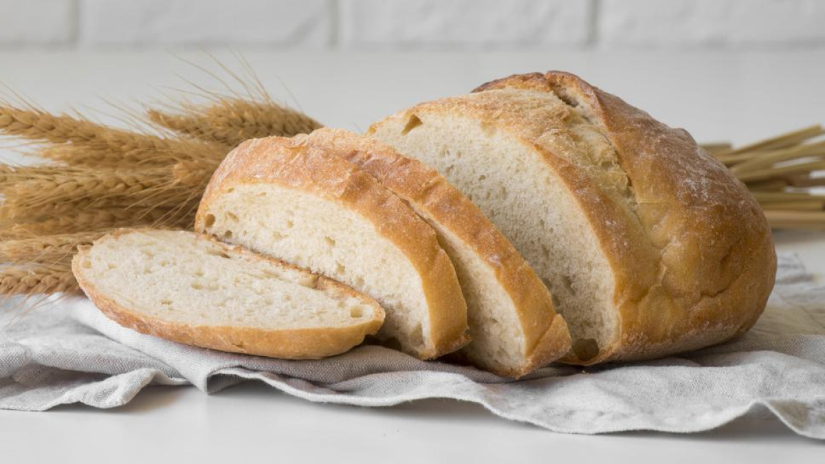 Pão caseiro fatiado em cima de pano branco com trigo ao redor
