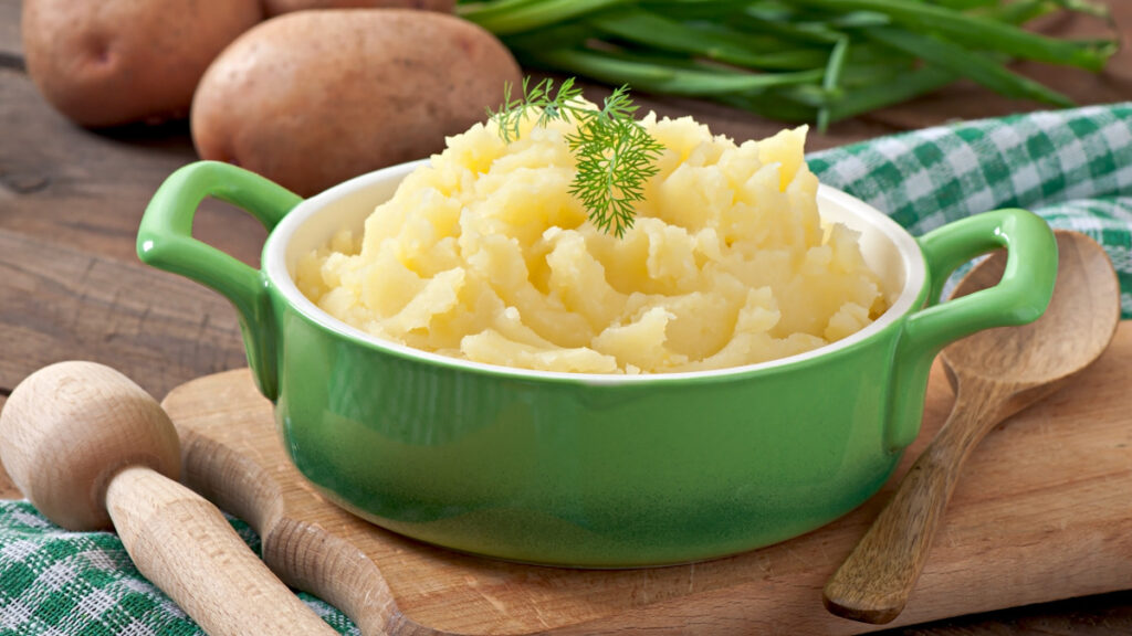 Purê de batatas servido em tigela tipo ramekin com folhas de coentro para decorar