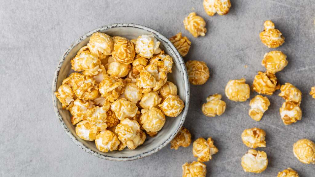 Pipoca caramelizada vista de cima em bowl branco e pipocas caídas ao lado