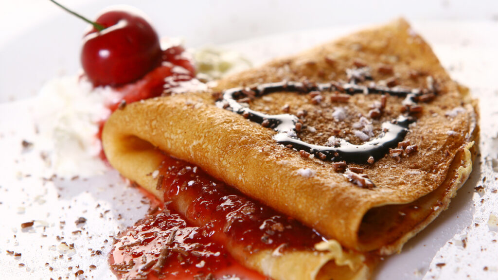 Crepe francês com recheio de chocolate por cima e cereja ao fundo