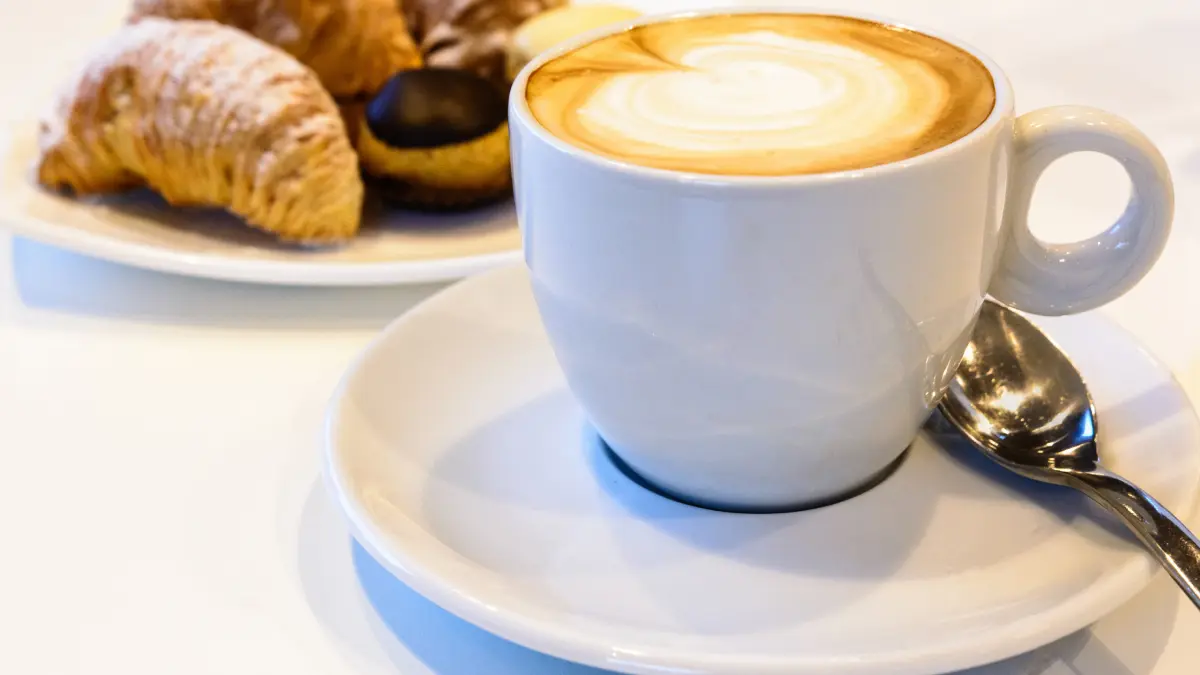 Cappuccino cremoso servido em xícara branca e um croissant ao lado
