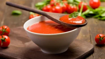 Molho de tomate caseiro servido em pote de vidro branco com uma colher de pau em cima