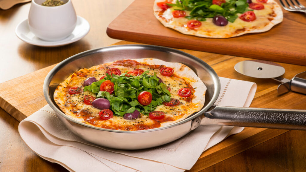 Pizza de frigideira em alumínio servida em cima de um pano sobre uma tábua de madeira