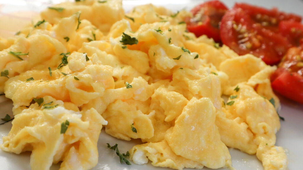 Ovos mexidos em prato branco com tomates ao lado