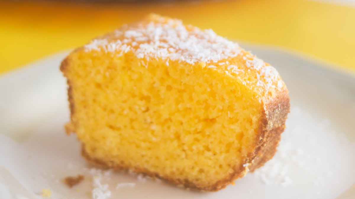 Fatia de bolo de milho de lata servido em um prato branco com polvilho de açúcar em cima