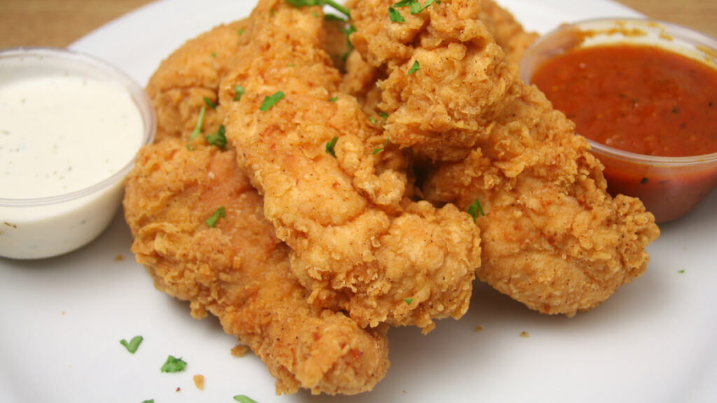 Frango empanado em prato branco com dois potinhos de molho branco e molho vermelho ao lado