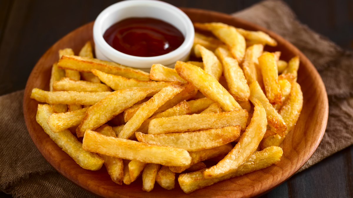 Batata frita servida em uma travessa de madeira com um potinho de ketchup do lado