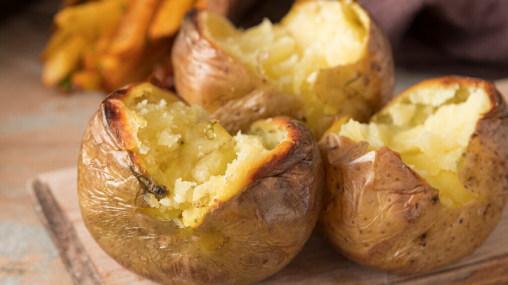 Três batatas ao murro abertas em cima de uma tábua de madeira