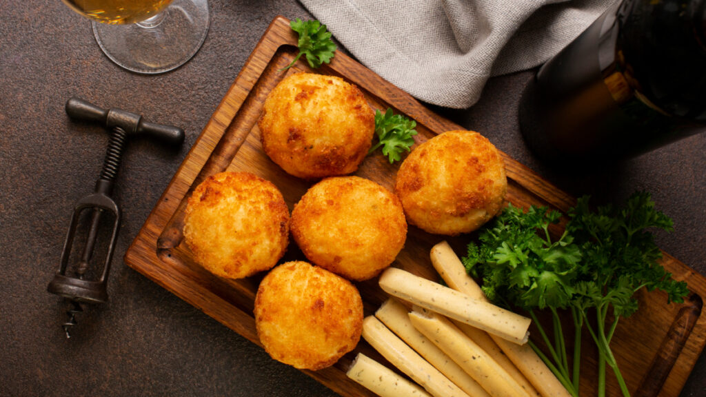 5 unidades de bolinho de bacalhau visto de cima em tábua de madeira