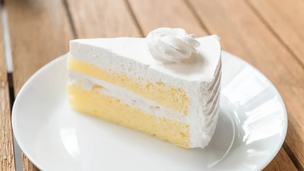 Fatia de bolo de leite ninho em prato branco redondo sobre uma mesa de madeira