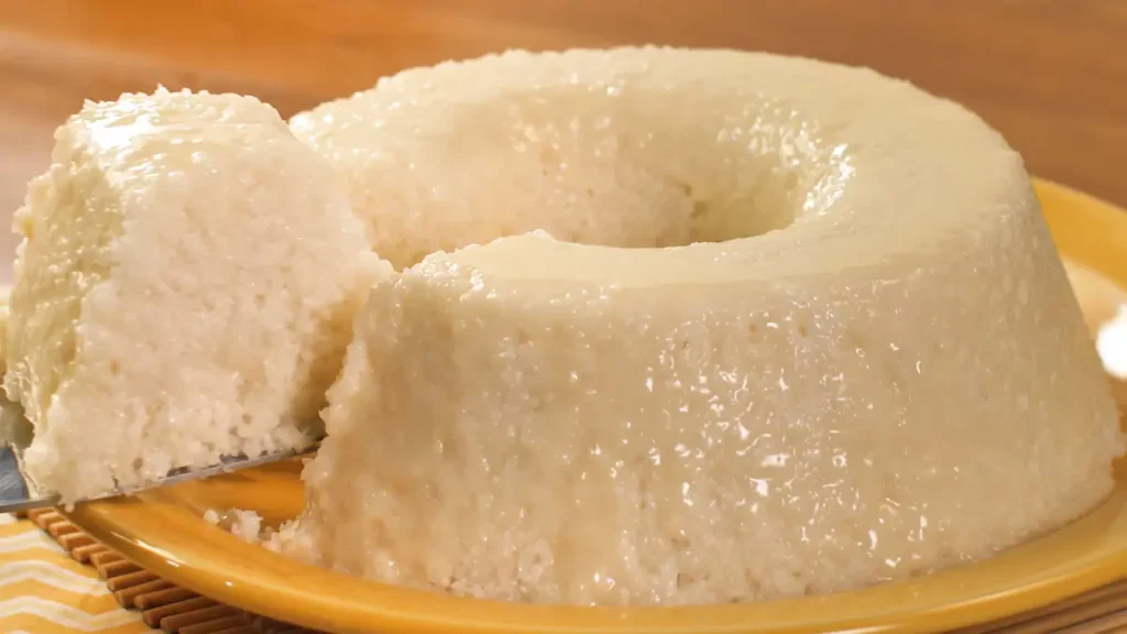 Fatia sendo retirada de um bolo de tapioca em cima de um prato amarelo