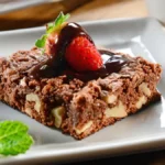 Brownie de nescau com morango e calda de chocolate servido em um prato branco quadrado