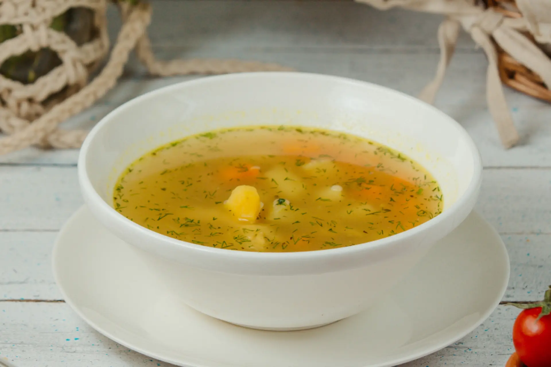 Sopa de legumes servida em bowl branco de porcenala em mesa de madeira.