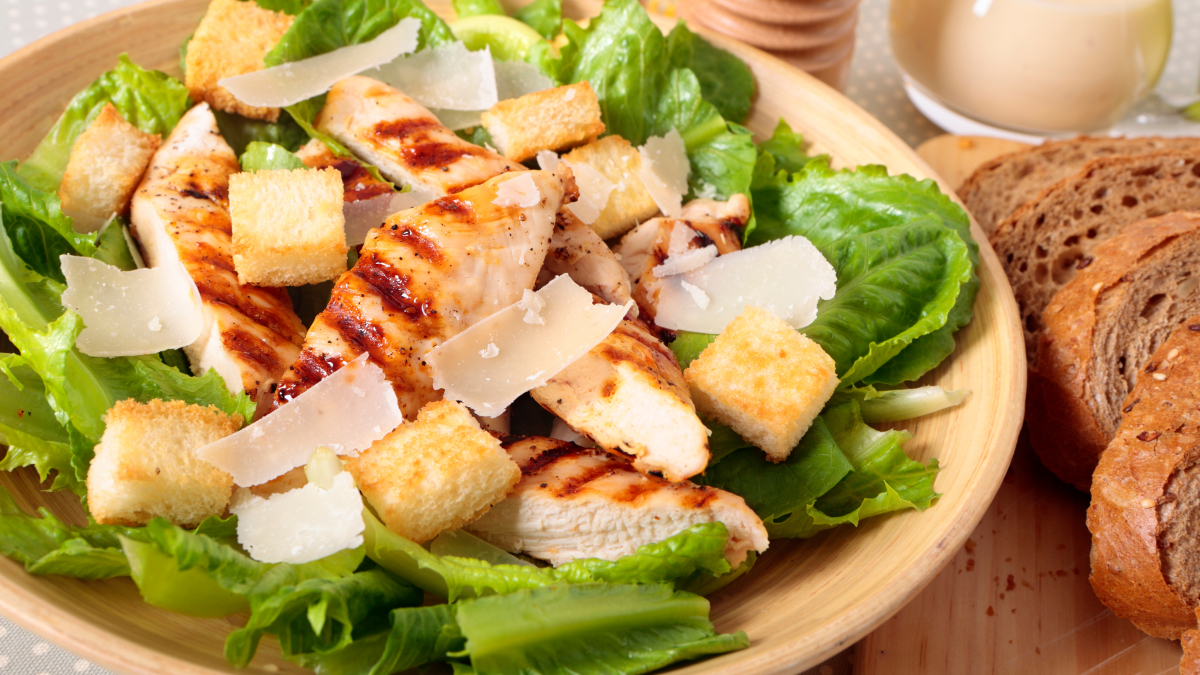 Salada Caesar servida em prato com filé de frango, pães torrados, alface e queijo