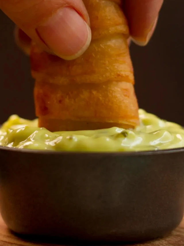 Mão colocando salgadinho dentro de maionese verde