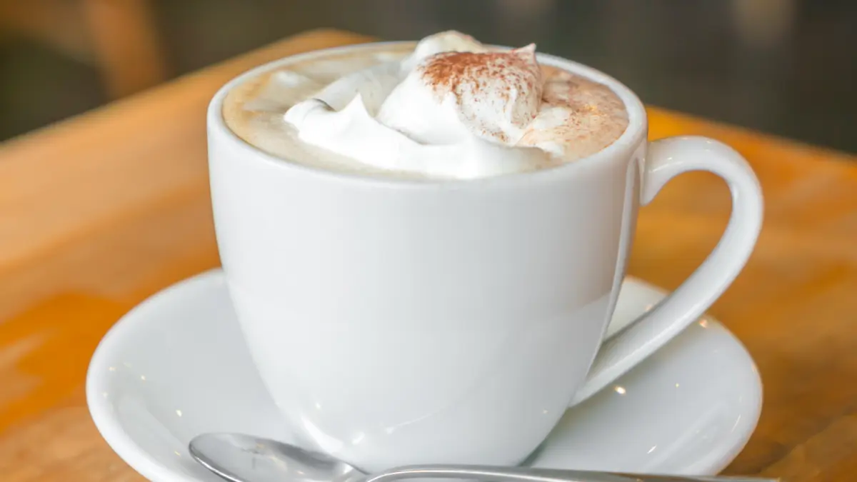 Café cremoso servido em xícara de vidro branca com canela