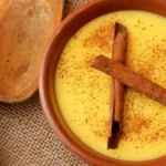 Curau de milho em bowl de cerâmica com canela em pó e pau de canela vista de cima