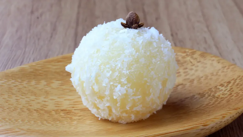 Beijinho de coco com cravo em cima de colher de pau visto de perto com mesa de madeira ao fundo