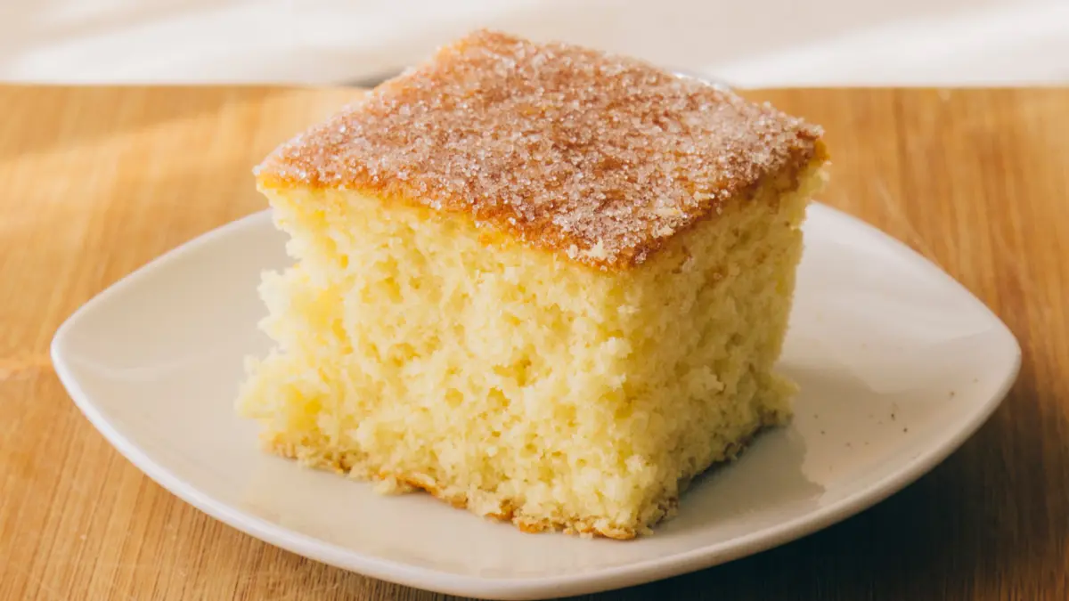 Fatia de bolo de fubá fofinho em prato branco viso de perto em cima de mesa de madeira