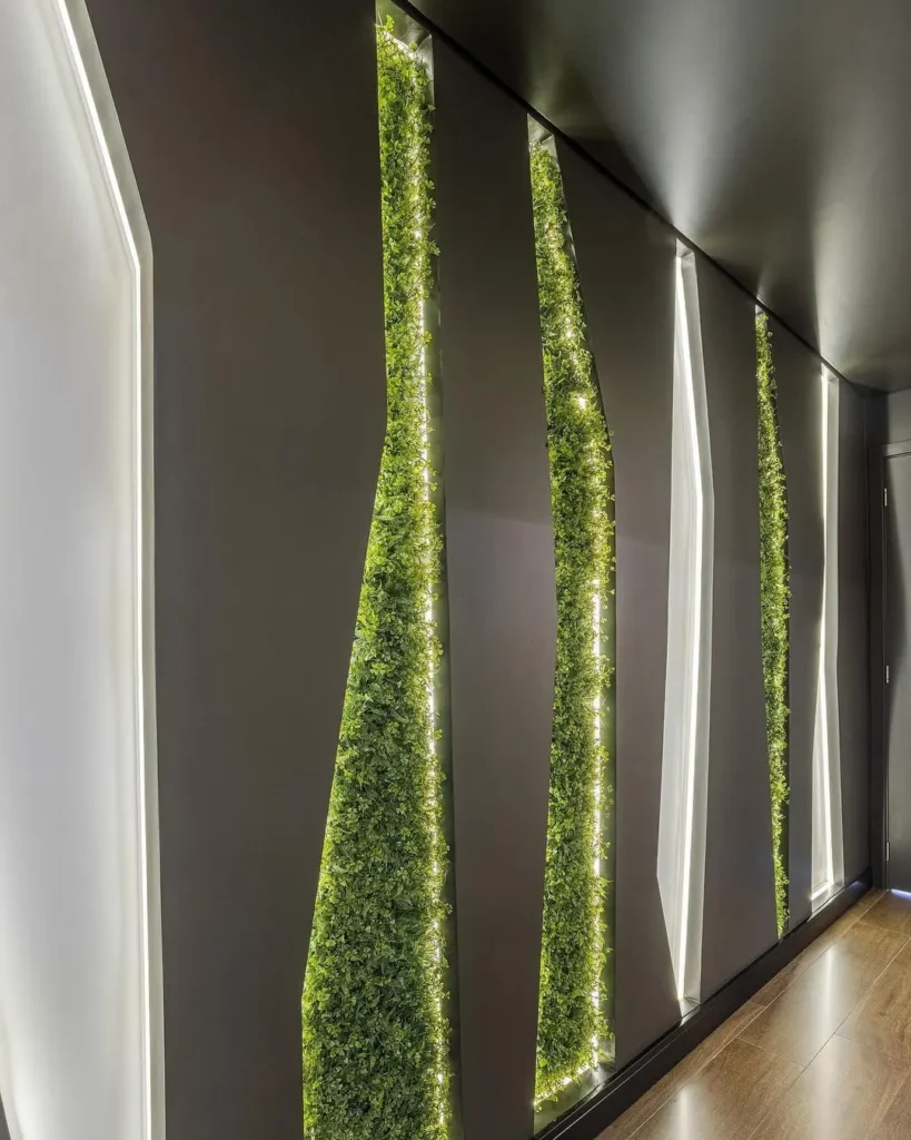 Tipo de jardim vertical em hall social, fazendo uma composição com painéis de MDF e luz indireta