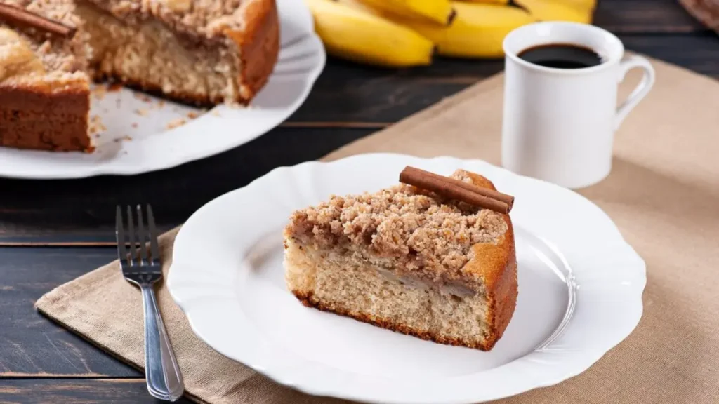 Fatia de bolo de banana fit em prato branco com caneca de café ao lado