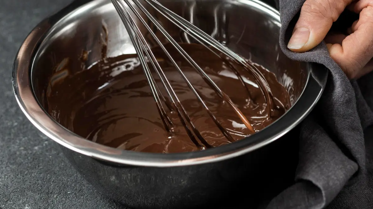 Ganache de chocolate em bowl de inox sendo mexido com fouet.