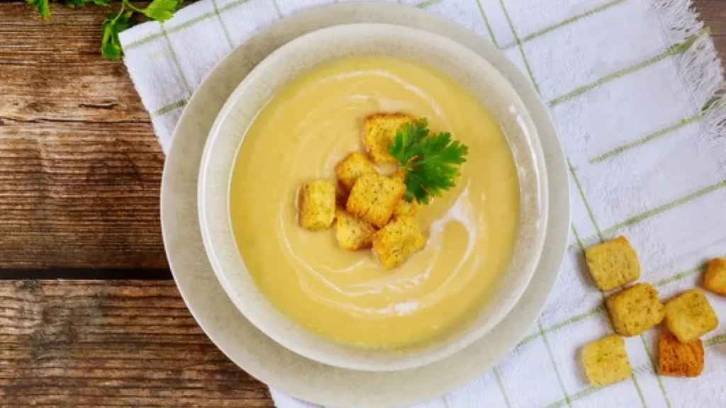 Sopa de mandioca em tigela branca vista de cima com croutons e salsinha