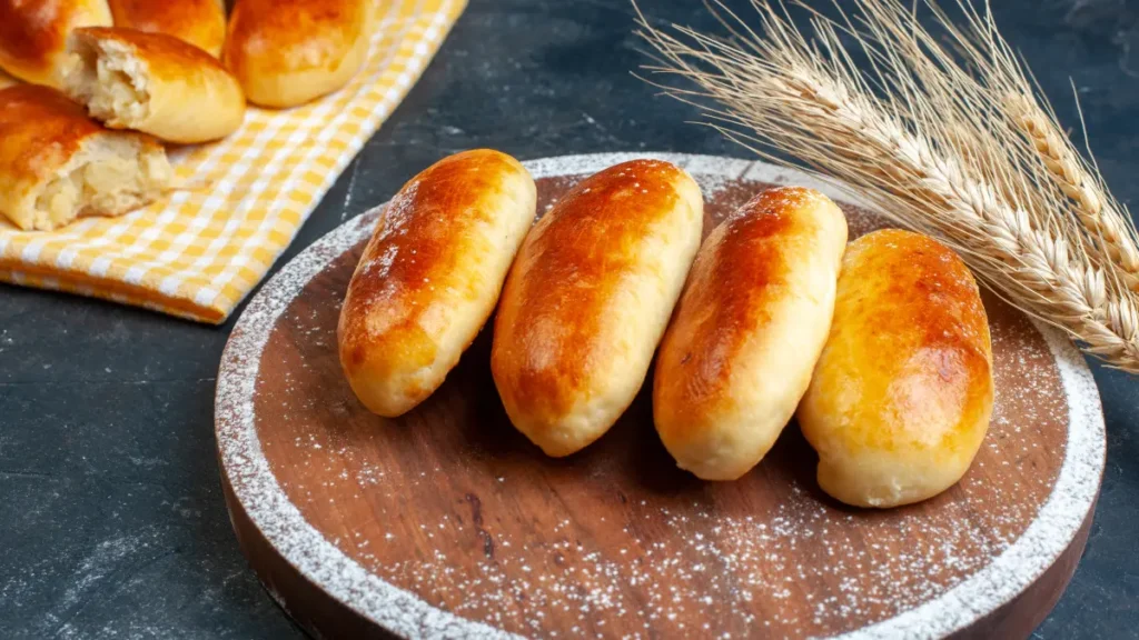 Pãozinho caseiro em tábua de madeira com trigo ao lado