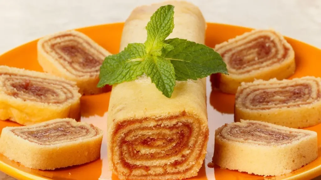 Bolo de rolo com uma folha de decoração no topo e ao lado pequenas fatias do bolo. Servido em um prato laranja.