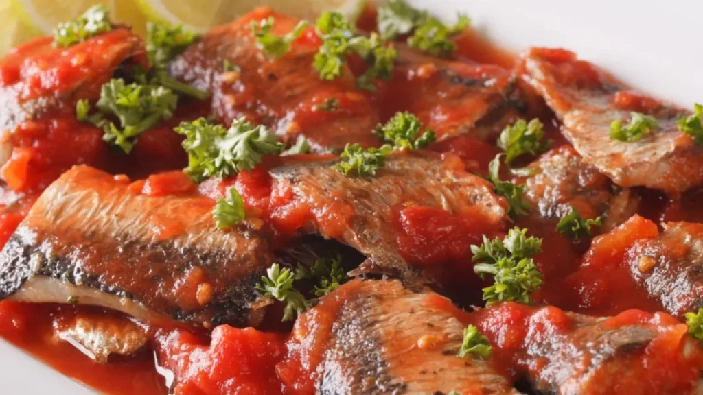 Sardinha de panela de pressão servida em prato com molho de tomate e pequenos pedaços de alface.