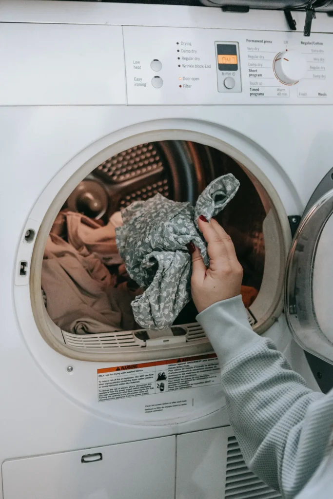 Pessoa adicionando roupas dentro da máquina de lavar com abertura frontal