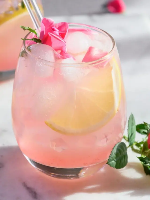 Pink lemonade servida em copo de vidro e decorada com limões e mini rosas