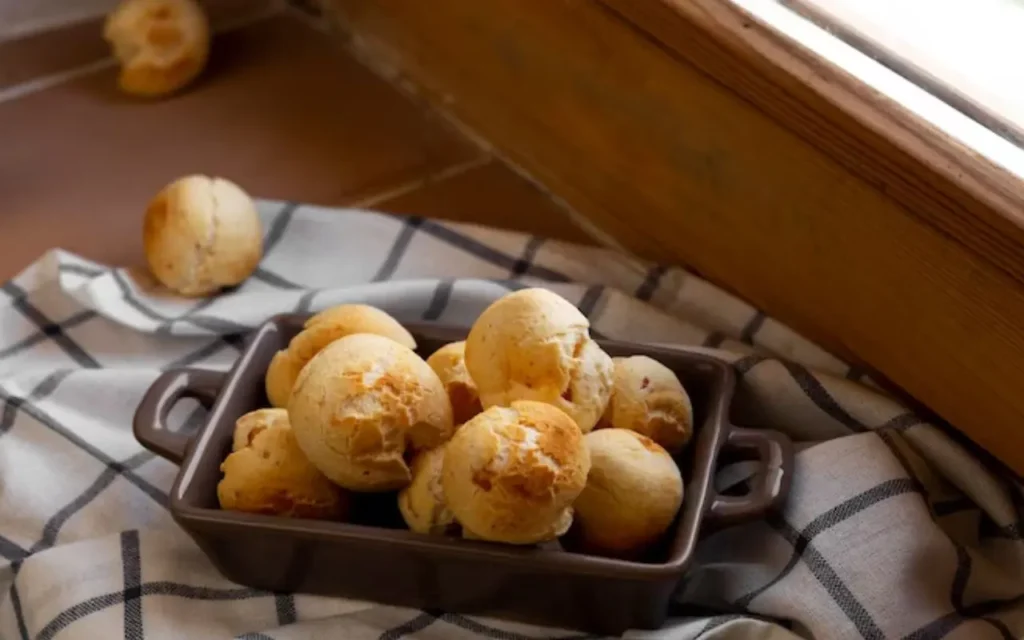 Pão de queijo de tapioca em travessa preta retangular em cima de pano com listras pretas