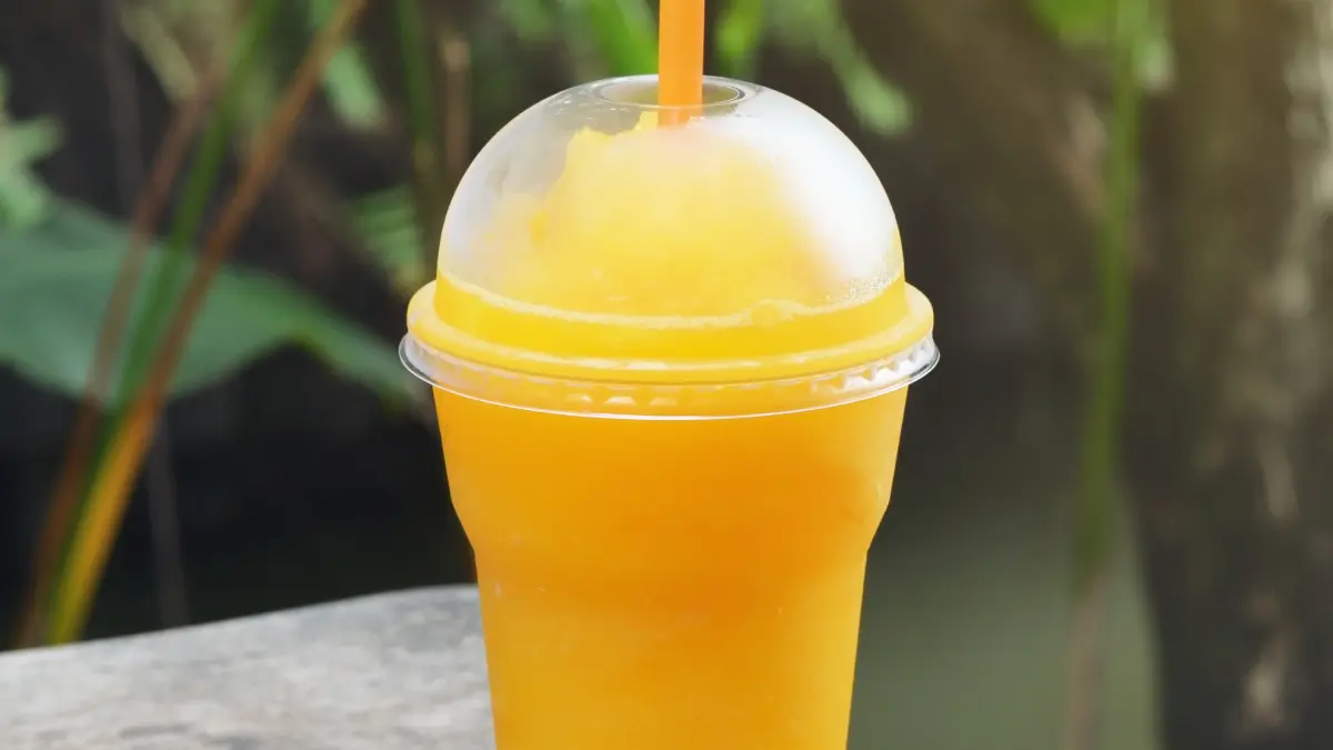 Frapê de laranja em copo de plástico com canudo