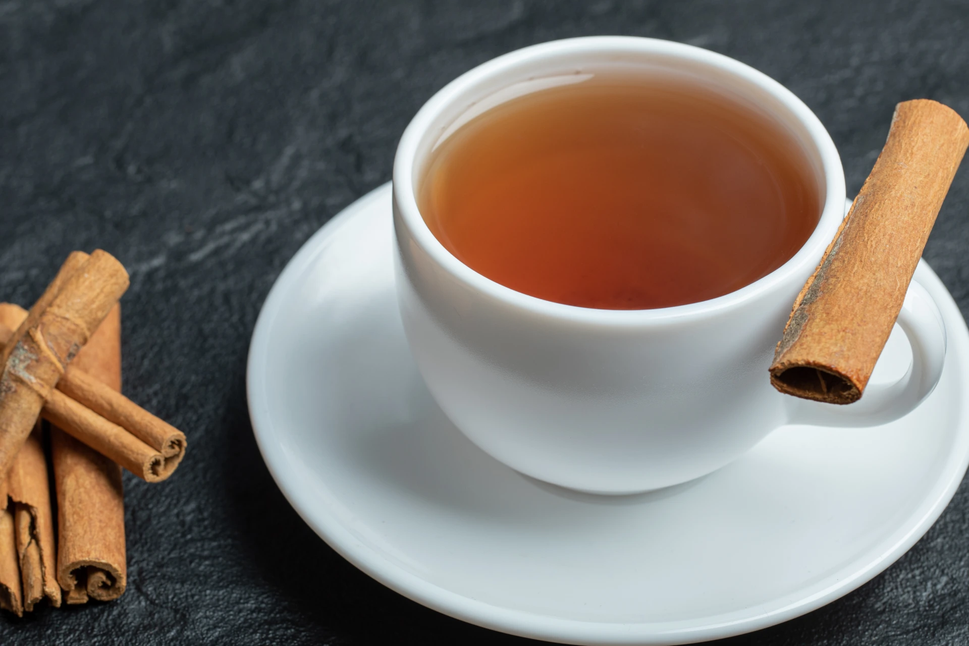 Chá de canela em xícara branca com detalhes de paus de canela.