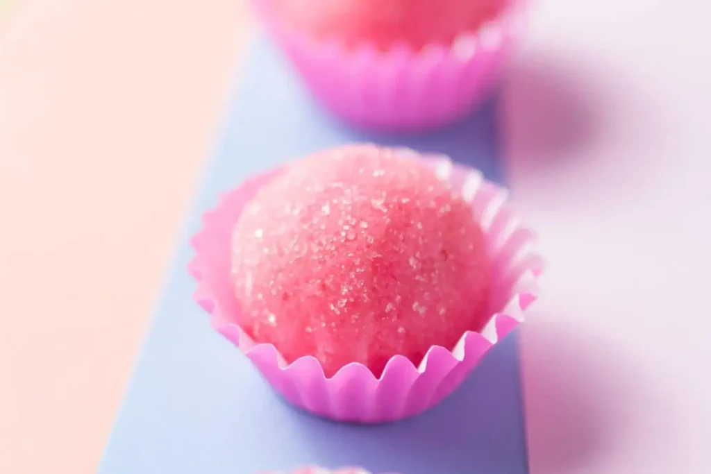 Docinho tipo brigadeiro cor de rosa, enrolado com açúcar, em forminha de papel cor de rosa.