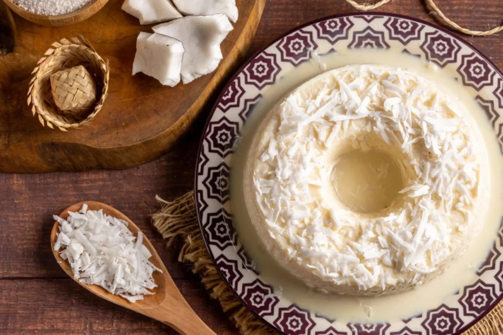 Bolo de tapioca em uma tigela com estampa colorida e colher com coco ralado.