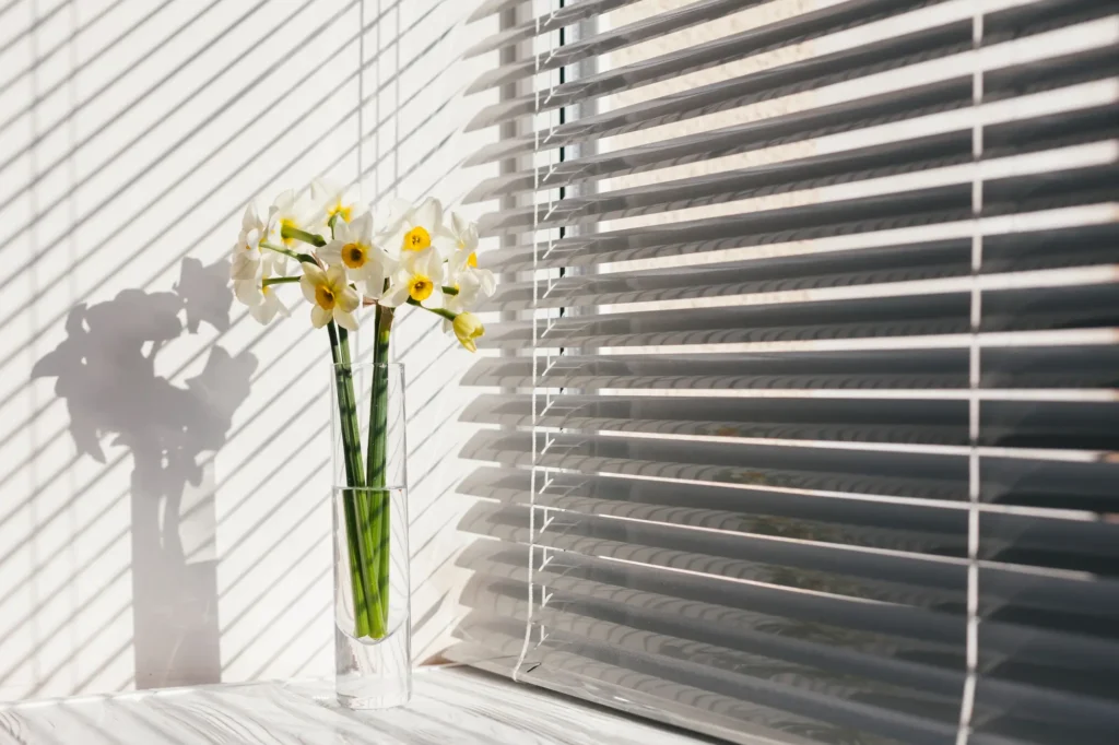 Persiana horizontal na cor branca em janela com um vaso de flores brancas ao lado