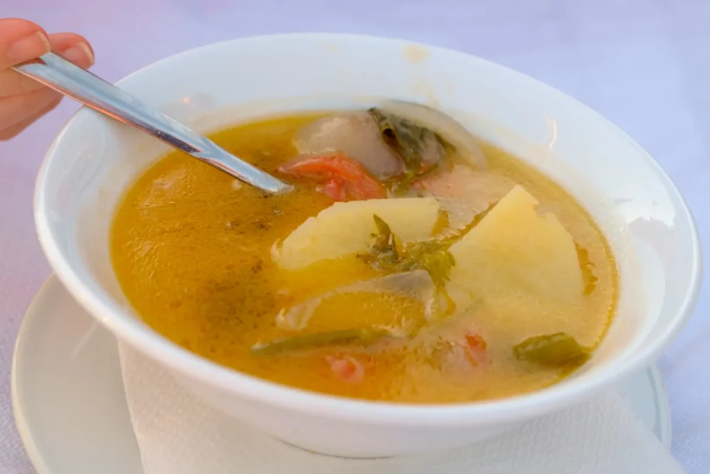 Uma sopa de peixe em prato fundo branco com colher dentro