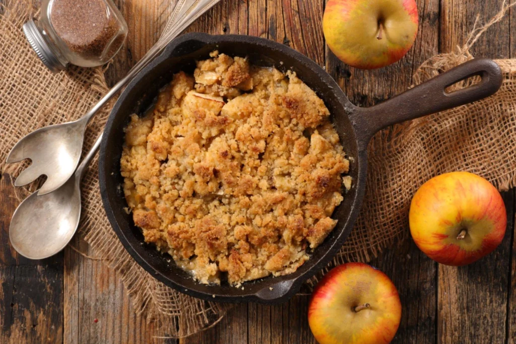 Crumble de maçã em panela com maças decorativas do lado.