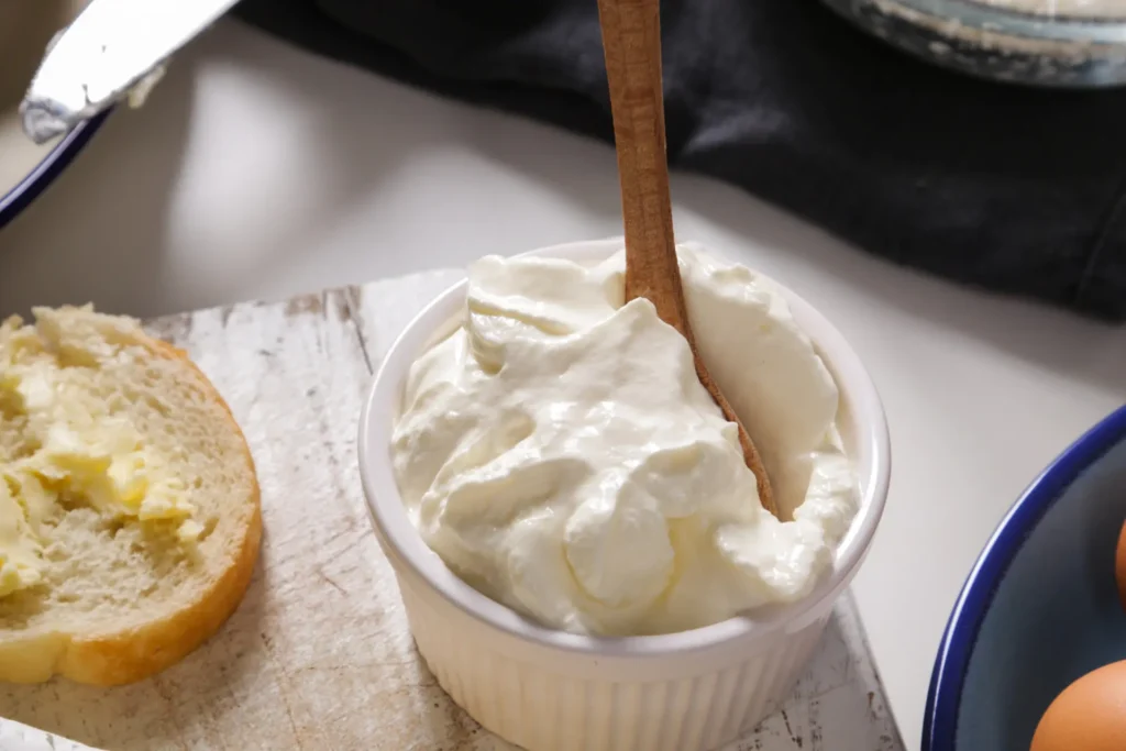 Requeijão caseiro em pote branco em uma mesa com vários alimentos